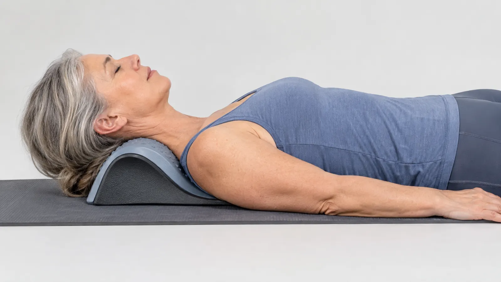 Woman in her fifties lying on an exercise mat with the Restcloud neck stretcher under her neck, eyes closed and relaxed