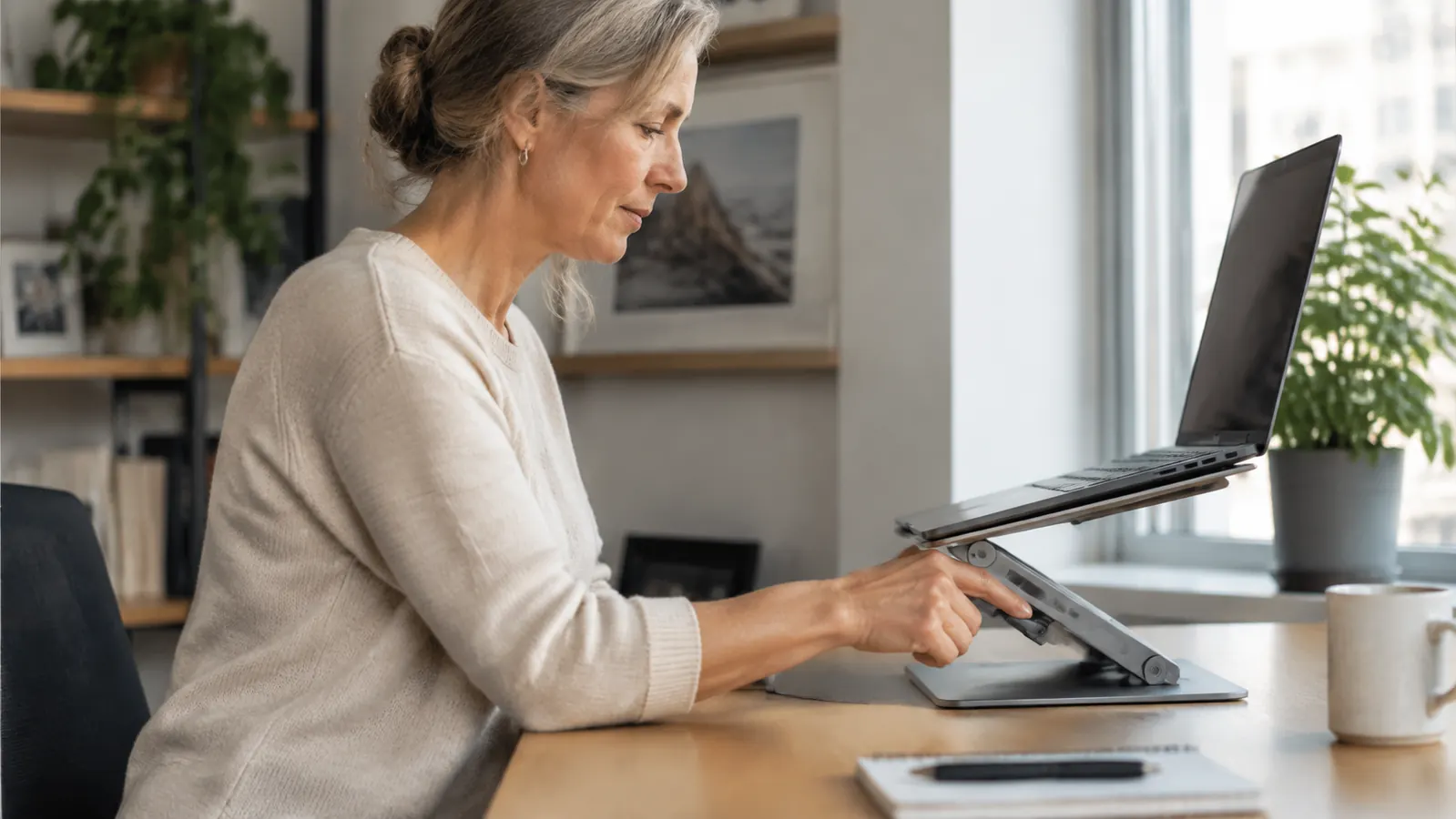 A woman in her fifties adjusting the height of a laptop stand at a desk